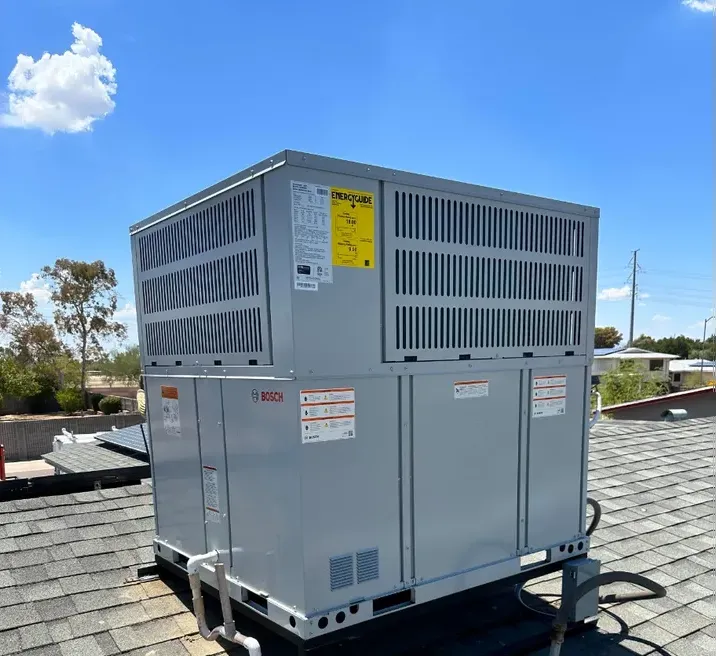A new packaged heating and cooling unit sitting on a shingle roof under a clear blue sky.